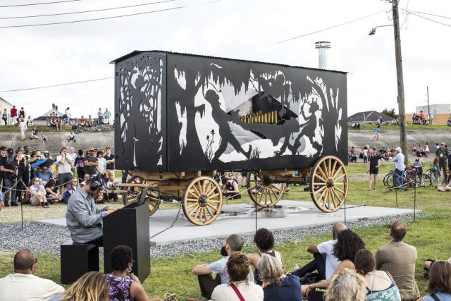 Kara Walker, The Katastwóf Karavan, 2017 (Installation view, Prospect.4: The Lotus in Spite of the Swamp, Prospect New Orleans, New Orleans, Louisiana, 2018). Steel frame mounted to lumber running gear, aluminum, red oak and muslin wall panels, propane fired boiler, water tank, gas generator, brass and steel 38-note steam calliope, calliope controller panel with MIDI interface, iPad controller with QRS PNO software; 152 × 216 × 100 inches (386.1 × 548.6 × 254 cm). © Kara Walker. Image courtesy Sikkema Jenkins & Co., New York. Photograph by Alex Marks